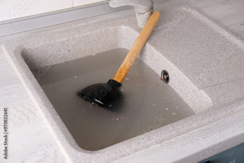 plunger with wooden handle lies in clogged sink in water, removing blockage photo