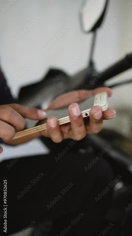 Male hand scrolls a smartphone. Close-up of man holding smartphone and scrolling through news social media feed while sitting in the motorbike. Male hand scrolls a smartphone. Close-up of man holding smartphone and scrolling through news social media feed while sitting in the motorbike.