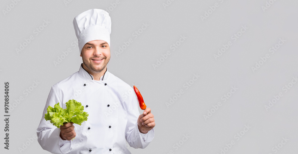 Male Chef Holding Red Pepper And Green Salad Leaves Smiling To Camera Standing Over Gray Studio Background. Panorama Male Chef Holding Red Pepper And Green Salad Leaves Smiling To Camera Standing Over Gray Studio Background. Panorama