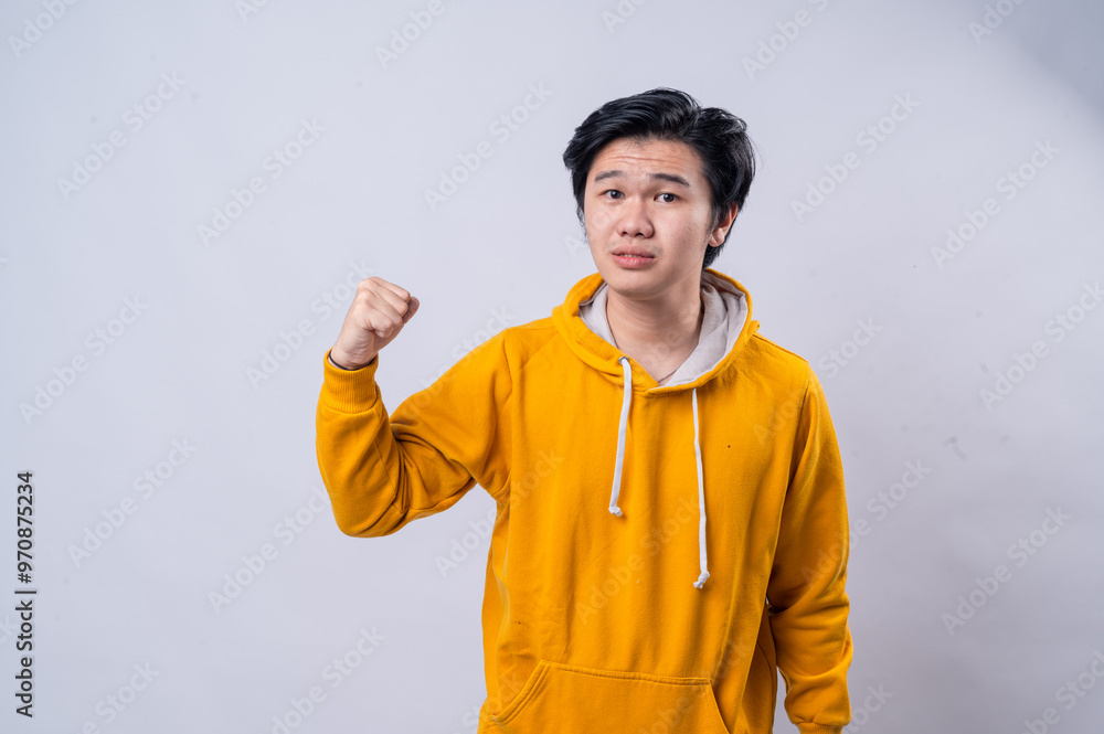 An Asian man in a yellow hoodie strikes a playful punch pose, looking focused while pointing toward the camera. He stands against a white background, showcasing energy and enthusiasm in a fun An Asian man in a yellow hoodie strikes a playful punch pose, looking focused while pointing toward the camera. He stands against a white background, showcasing energy and enthusiasm in a fun