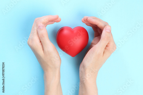 Woman holding red heart on light blue background, top view