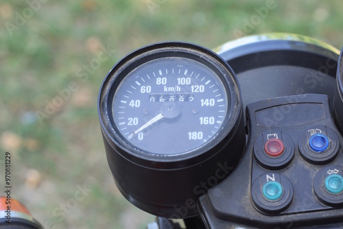 one black round plastic speedometer on the dashboard of an old motorcycle on a summer street