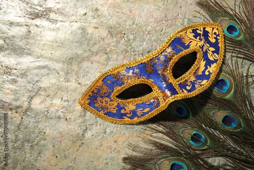 Beautiful bright carnival mask and peacock feathers on gray textured table, top view. Space for text photo