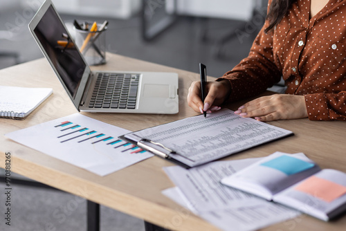Photos Hands of financier close-up, female accountant on paper work, fills forms, and enters data into forms, reconciles financial reports, uses calculator and laptop, writes reconciliation results