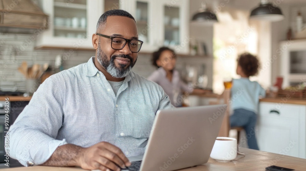 Smiling plus-size black man working on laptop at home with family in the background Smiling plus-size black man working on laptop at home with family in the background