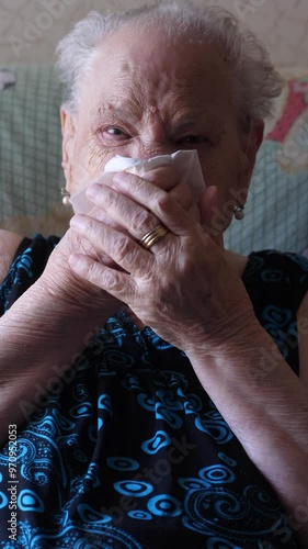 Vertical video of an 90-year-old woman sitting on the couch blowing her nose. A tender moment showcasing her everyday life photo