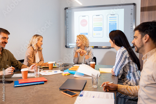 Group of business people sitting in a meeting room discussing a design for a smartphone application.