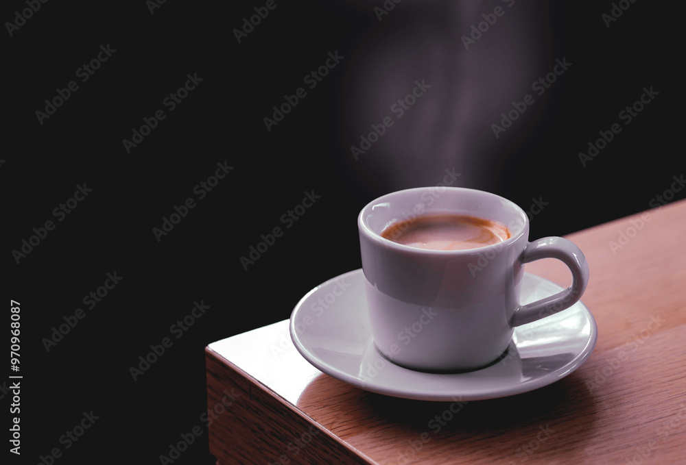 Side view a cup of hot coffee with steaming above the cup setting on wooden table against morning light on dark background, coffee background with copy space peaceful relaxing moment concept. Side view a cup of hot coffee with steaming above the cup setting on wooden table against morning light on dark background, coffee background with copy space peaceful relaxing moment concept.