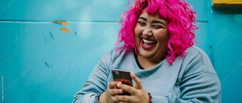 A woman with vibrant pink hair shares a hearty laugh while looking at her phone, sitting against a teal-colored background. A woman with vibrant pink hair shares a hearty laugh while looking at her phone, sitting against a teal-colored background.