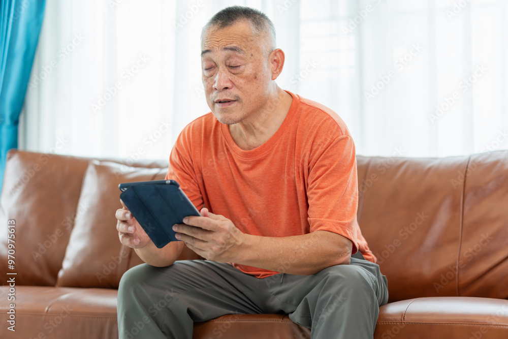 Senior man sitting on sofa and using digital tablet in living room Senior man sitting on sofa and using digital tablet in living room