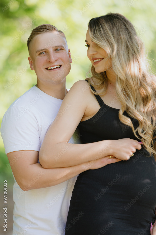 Fototapeta premium a man is hugging a pregnant woman in a black dress