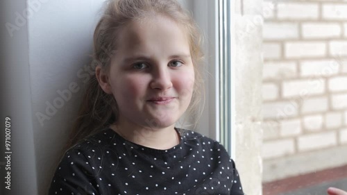 Teenage girl sits on the windowsill and talks. Little girl in a black dress with white polka dots, says something to the camera with a smile. Child's conversation