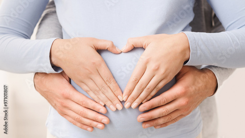 Loving couple making heart shape on pregnant belly with their hands, closeup