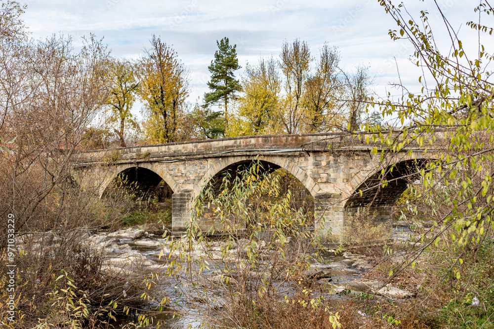 Fototapeta premium Old stone bridge over the river. Autumn perspective, details from the streets of Debnevo, village in Northern Bulgaria