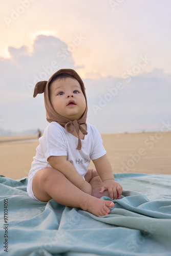a baby sitting on a blanket on the beach