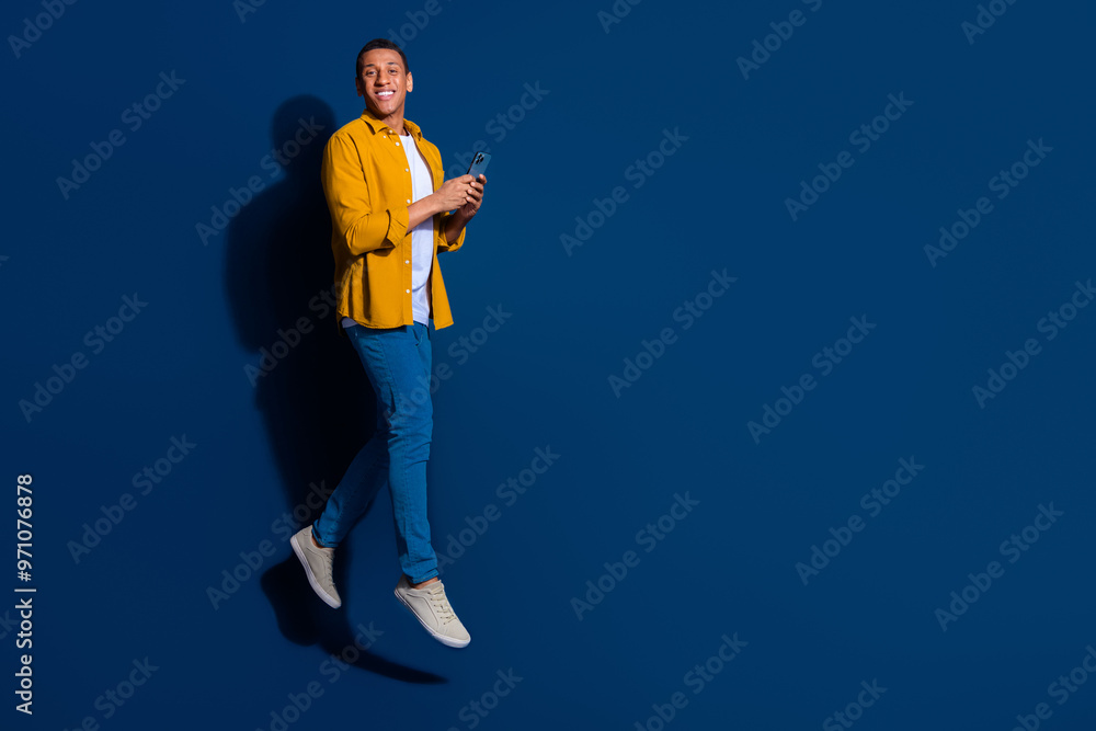 Full body length photo of young student man jumping using his smartphone searching cafe place isolated on dark blue color background Full body length photo of young student man jumping using his smartphone searching cafe place isolated on dark blue color background