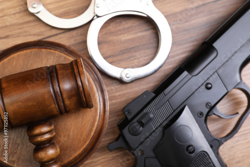 Judge's gavel, handcuffs and gun on wooden table, flat lay photo