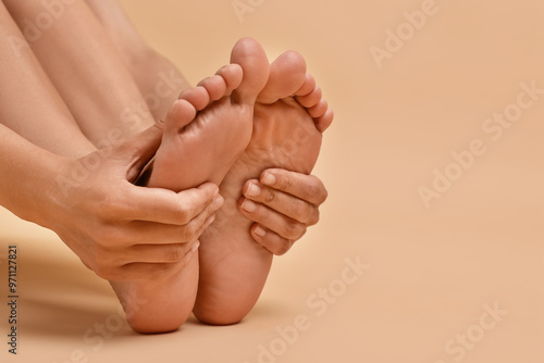 Woman touching her smooth feet on beige background, closeup. Space for text photo