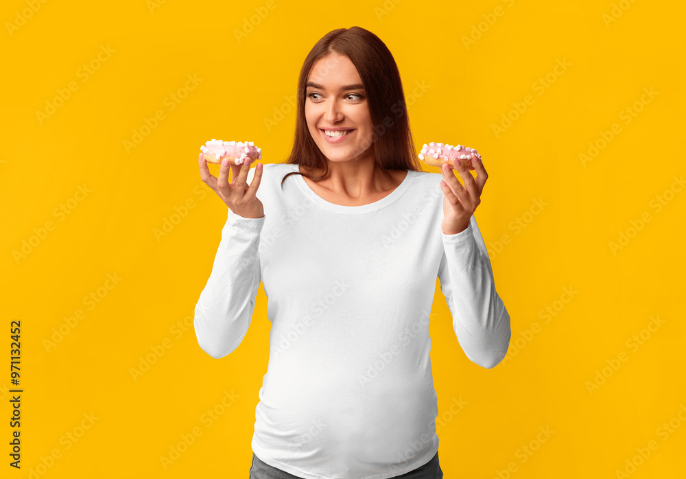 Unhealthy Food In Pregnancy. Hungry Pregnant Girl Holding Donuts Standing On Pink Background. Studio Shot Unhealthy Food In Pregnancy. Hungry Pregnant Girl Holding Donuts Standing On Pink Background. Studio Shot
