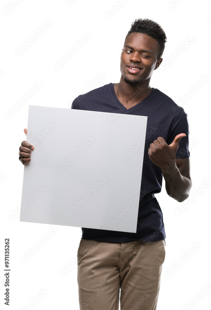 Young african american man holding a banner pointing with hand and finger up with happy face smiling Young african american man holding a banner pointing with hand and finger up with happy face smiling