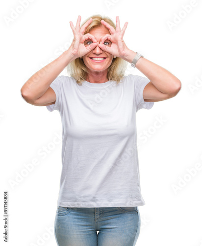 Middle age blonde woman over isolated background doing ok gesture like binoculars sticking tongue out, eyes looking through fingers. Crazy expression.