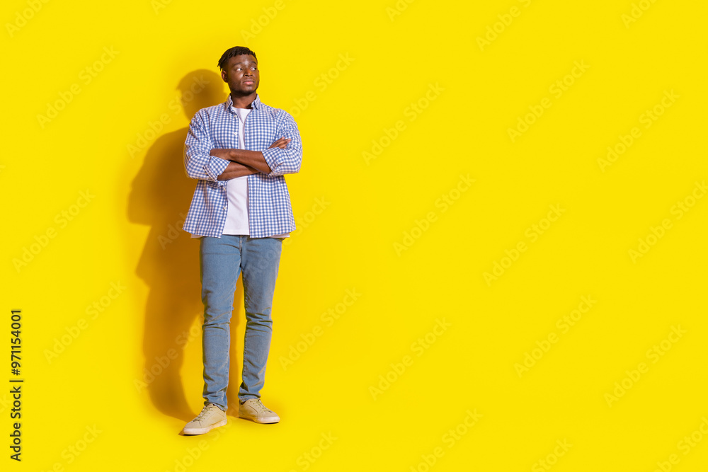 Full length photo of funky cool guy dressed checkered shirt hands crossed looking emtpy space isolated yellow color background Full length photo of funky cool guy dressed checkered shirt hands crossed looking emtpy space isolated yellow color background