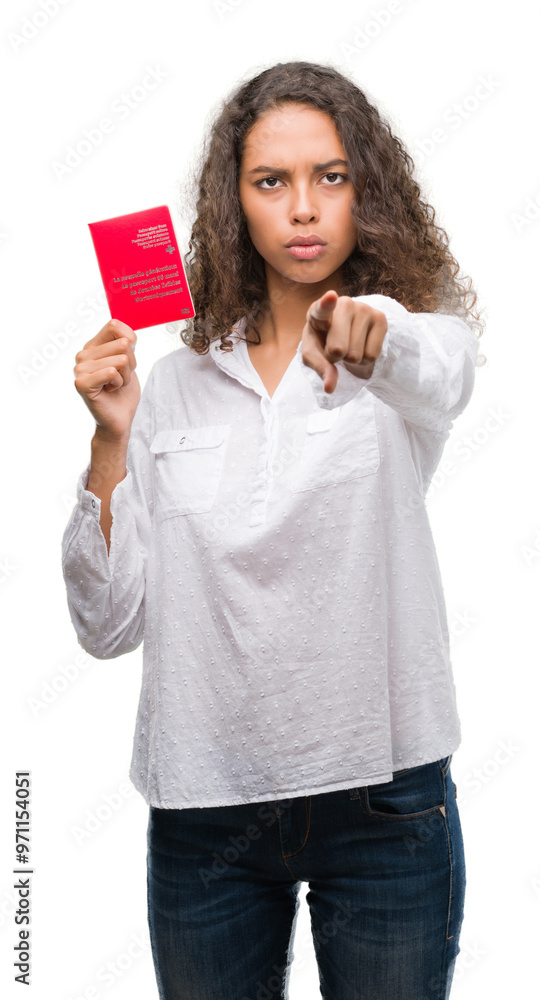 Young hispanic woman holding passport of Switzerland pointing with finger to the camera and to you, hand sign, positive and confident gesture from the front Young hispanic woman holding passport of Switzerland pointing with finger to the camera and to you, hand sign, positive and confident gesture from the front