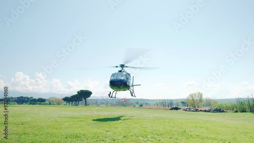 Helicopter with pilot and passengers landing on countryside field in sunny day, aircraft with rotating blades hovering above green lawn, helicopter flying experience concept