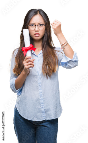 Young asian woman holding degree over isolated background annoyed and frustrated shouting with anger, crazy and yelling with raised hand, anger concept