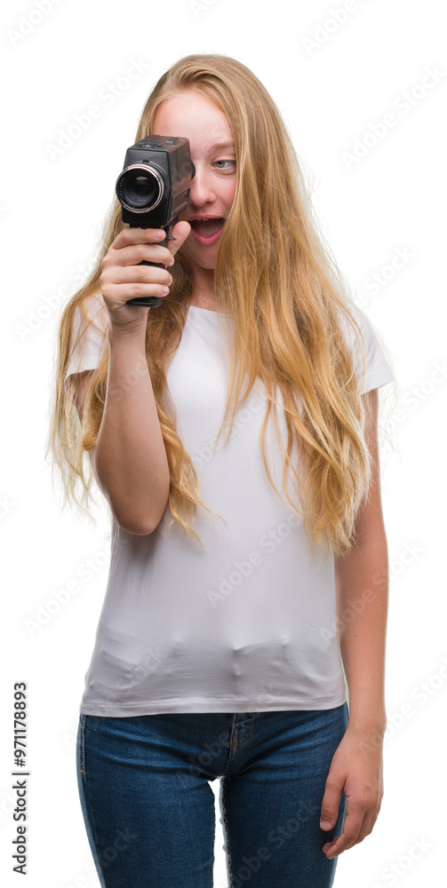Blonde woman teenager filming holding super 8 video camera scared in shock with a surprise face, afraid and excited with fear expression Blonde woman teenager filming holding super 8 video camera scared in shock with a surprise face, afraid and excited with fear expression