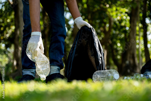 Hand holding plastic bottle waste, picking up trash and putting it in the black garbage bag at the Park on Environmental Earth day photo