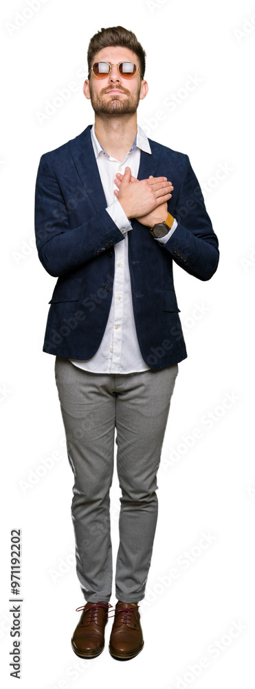Young handsome elegant man wearing sunglasses and fashion blazer smiling with hands on chest with closed eyes and grateful gesture on face. Health concept. Young handsome elegant man wearing sunglasses and fashion blazer smiling with hands on chest with closed eyes and grateful gesture on face. Health concept.