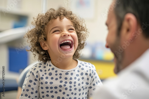 A cheerful young child laughs as the doctor gently examines their throat with a tongue depressor in a friendly, well-decorated examination room. The child is seated comfortably on the exam table, and