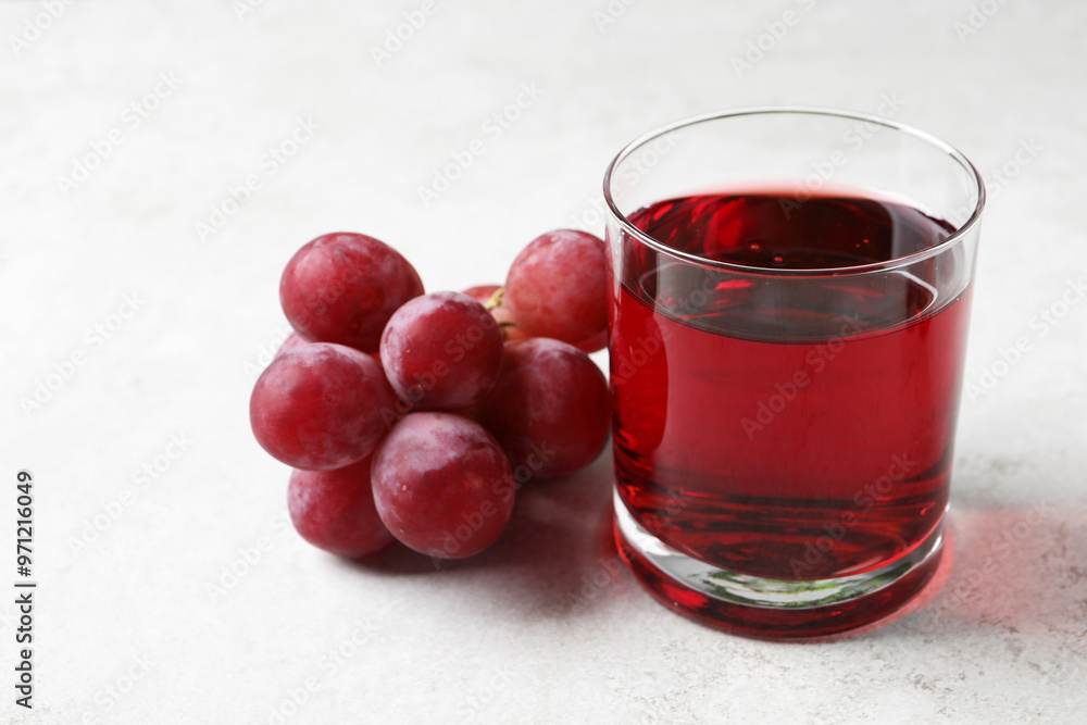 Tasty grape juice in glass and berries on light textured table, closeup Tasty grape juice in glass and berries on light textured table, closeup