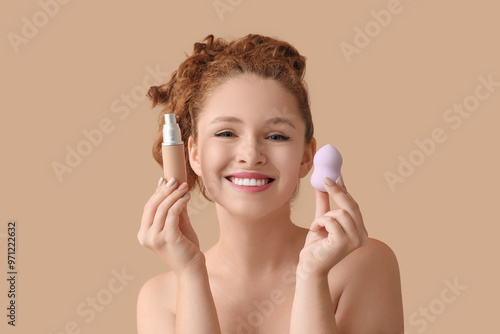 Young redhead woman with makeup foundation and sponge on beige background, closeup photo