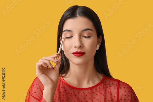 Beautiful young woman applying stylish eyeshadows on yellow background