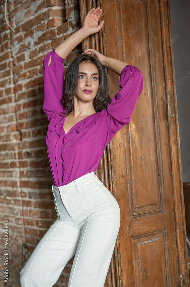 Beautiful young brunette woman in a purple blouse and white pants posing outdoor. Portrait of a beautiful young brunette woman with long hair posing fashion