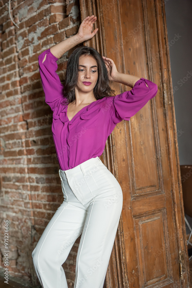Beautiful young brunette woman in a purple blouse and white pants posing outdoor. Portrait of a beautiful young brunette woman with long hair posing fashion