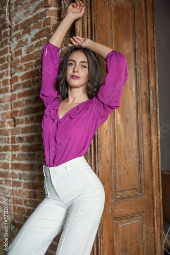 Obraz na płótnie Beautiful young brunette woman in a purple blouse and white pants posing outdoor. Portrait of a beautiful young brunette woman with long hair posing fashion w salonie