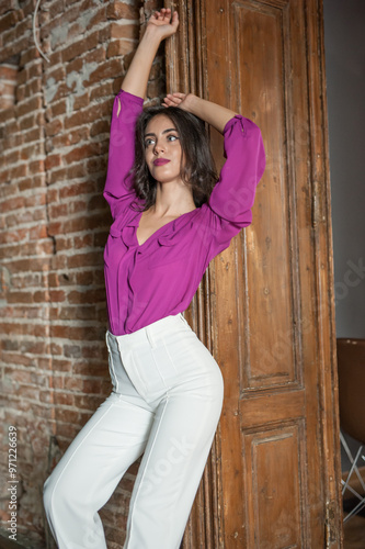 Obraz na płótnie Beautiful young brunette woman in a purple blouse and white pants posing outdoor. Portrait of a beautiful young brunette woman with long hair posing fashion w salonie