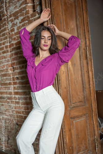 Obraz na płótnie Beautiful young brunette woman in a purple blouse and white pants posing outdoor. Portrait of a beautiful young brunette woman with long hair posing fashion w salonie