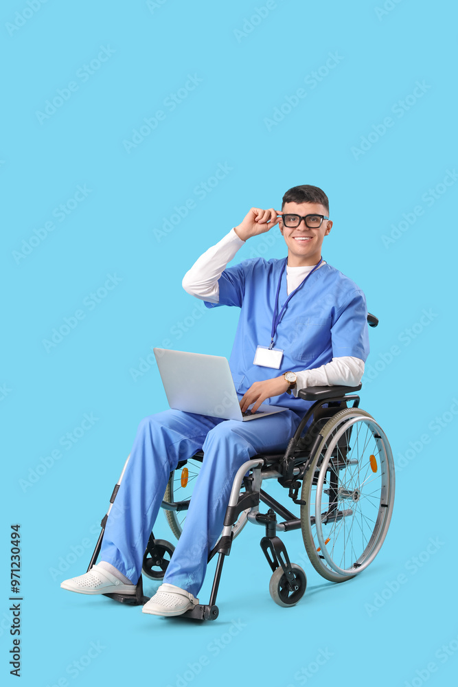 Young male doctor in wheelchair with laptop on blue background Young male doctor in wheelchair with laptop on blue background