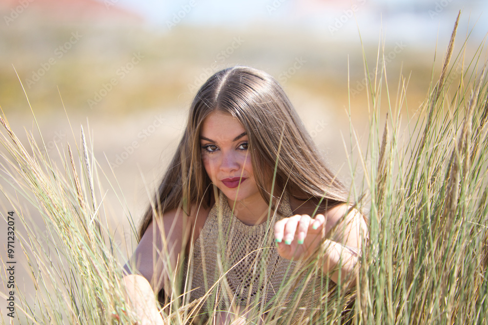 A pretty young woman with long hair waves her hands away and peers out from behind the reeds over some fine golden sand dunes. The woman is wearing make-up and is on holiday in andalusia, Spain. A pretty young woman with long hair waves her hands away and peers out from behind the reeds over some fine golden sand dunes. The woman is wearing make-up and is on holiday in andalusia, Spain.
