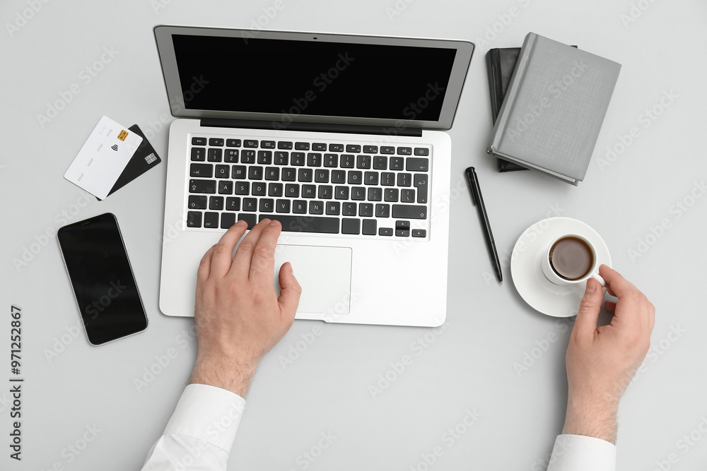 Male hands with laptop, mobile phone, credit cards and cup of coffee on grey background Male hands with laptop, mobile phone, credit cards and cup of coffee on grey background