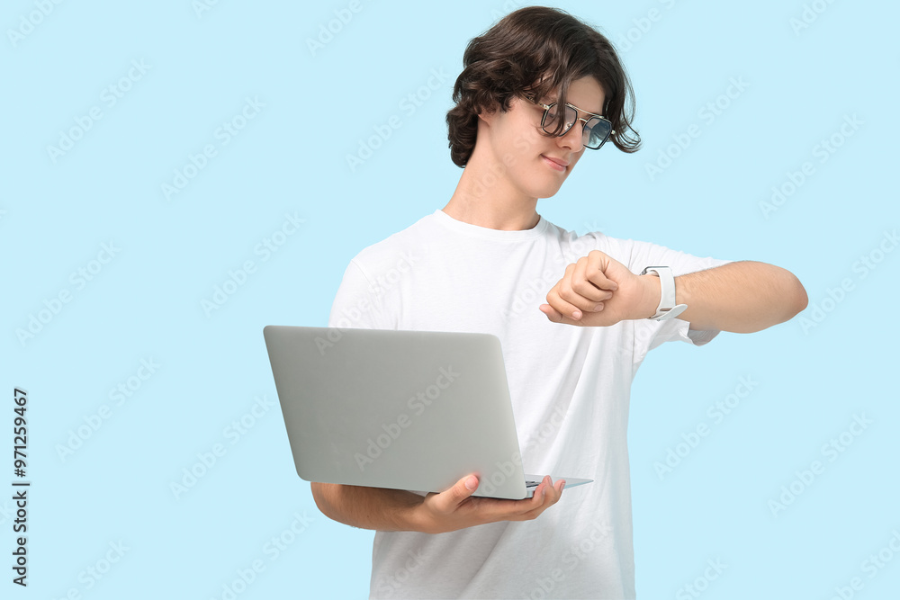 Male programmer in eyeglasses with laptop looking at wristwatch on blue background Male programmer in eyeglasses with laptop looking at wristwatch on blue background