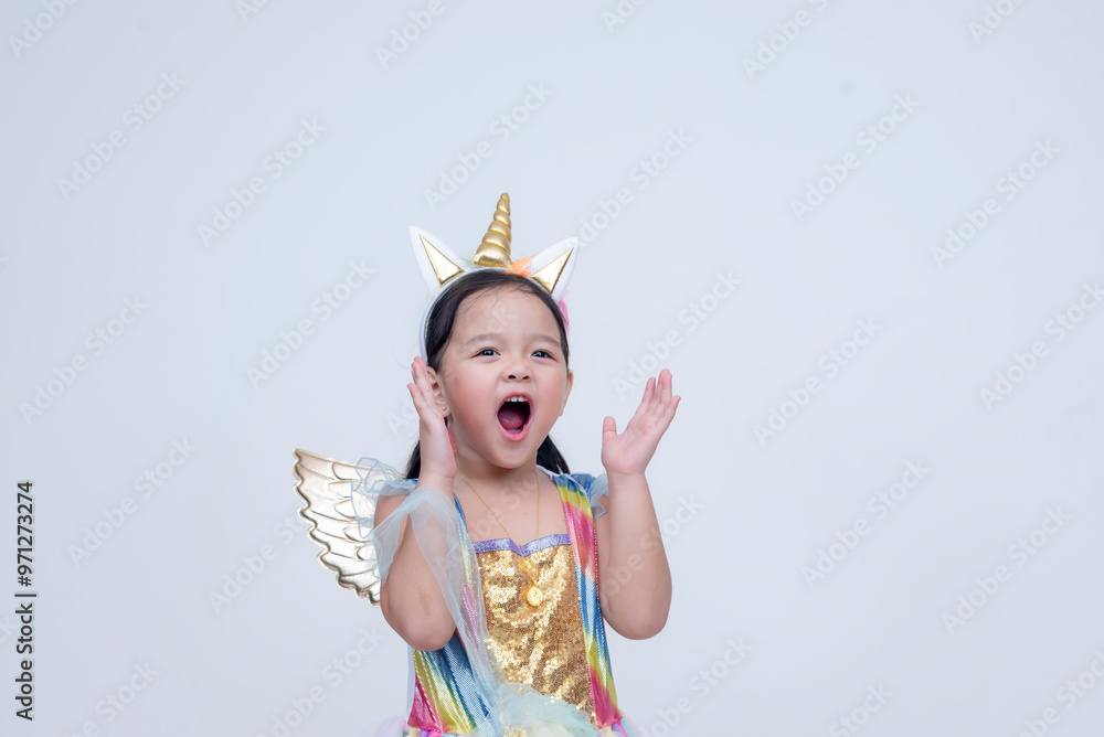 A young girl dressed in a vibrant unicorn costume expresses excitement, with wide eyes and an open mouth. Isolated on a white background. A young girl dressed in a vibrant unicorn costume expresses excitement, with wide eyes and an open mouth. Isolated on a white background.