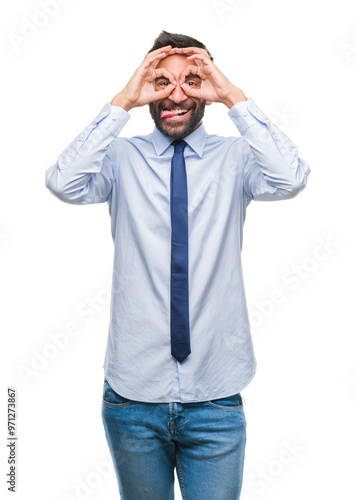 Adult hispanic business man over isolated background doing ok gesture like binoculars sticking tongue out, eyes looking through fingers. Crazy expression.