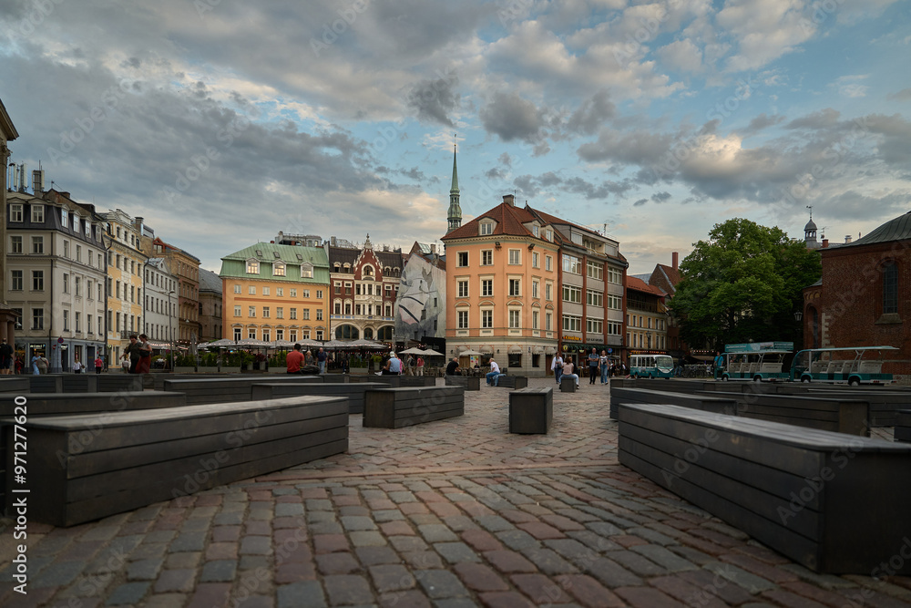 Fototapeta premium A bustling scene unfolds in Riga's iconic Dome Square, featuring historic buildings, a charming statue, and locals enjoying the lively atmosphere.