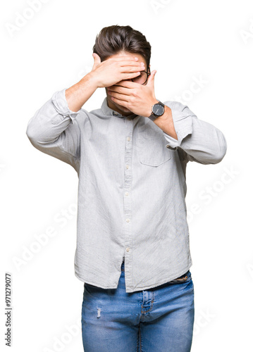 Young handsome man wearing glasses over isolated background Covering eyes and mouth with hands, surprised and shocked. Hiding emotion