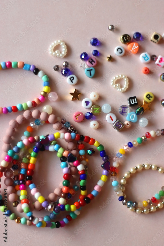 Colorful DIY necklaces, friendship bracelets and various plastic beads on pastel pink background. Flat lay.